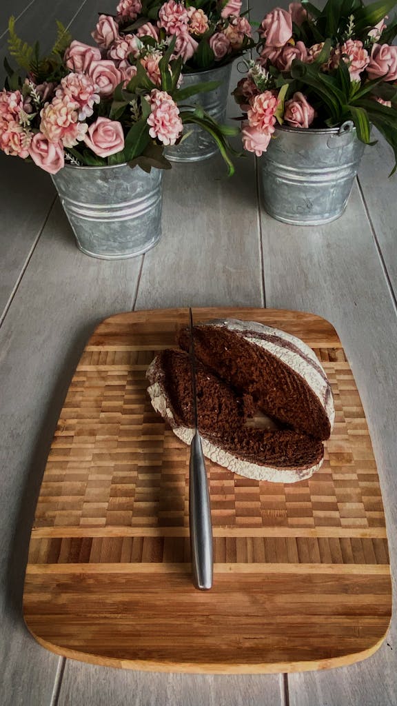 A rustic setup of sliced brown bread on a wooden board with pink flowers in metal buckets.