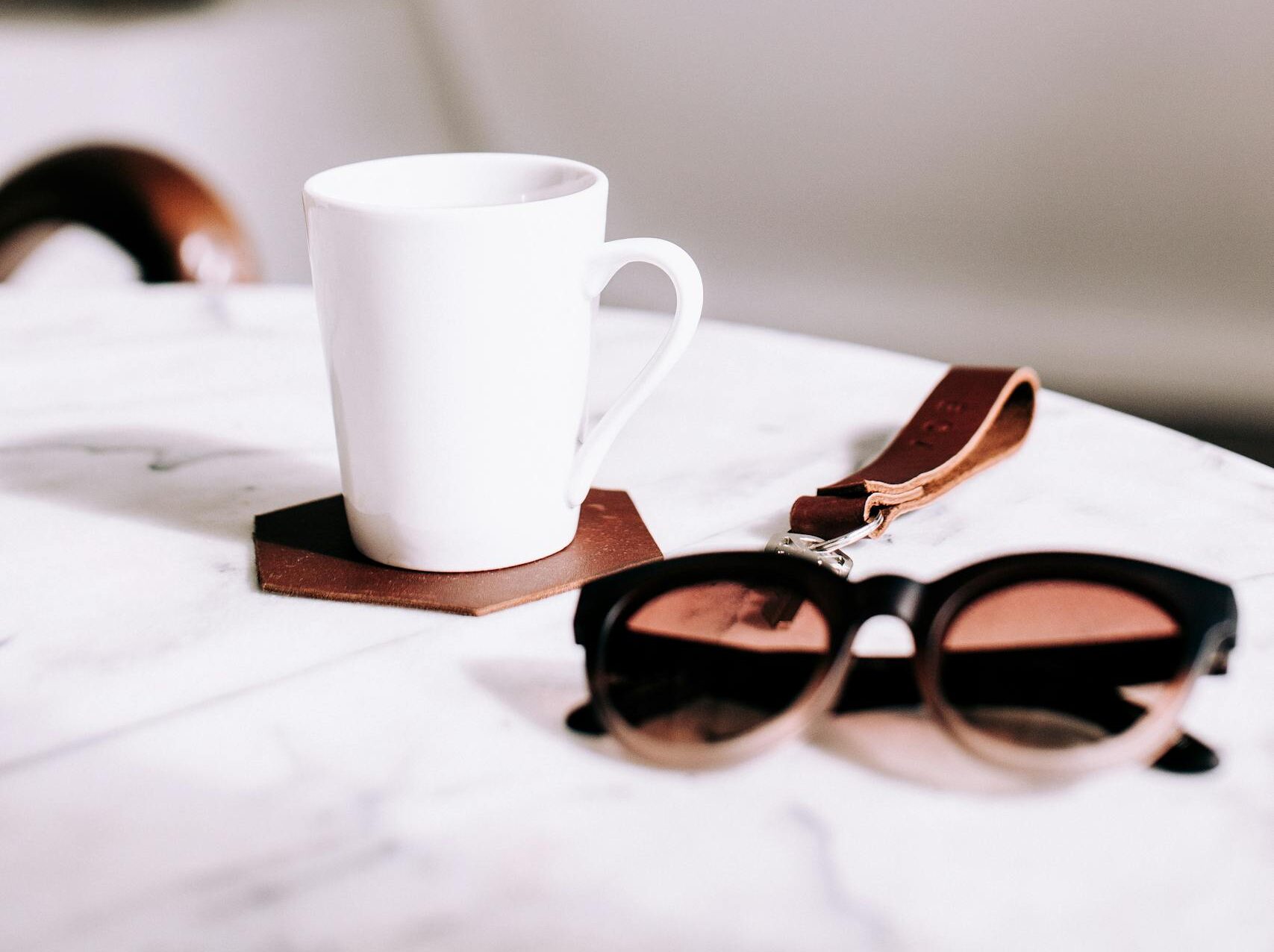 A simple yet stylish coffee setup featuring a ceramic mug on a marble surface with sunglasses.