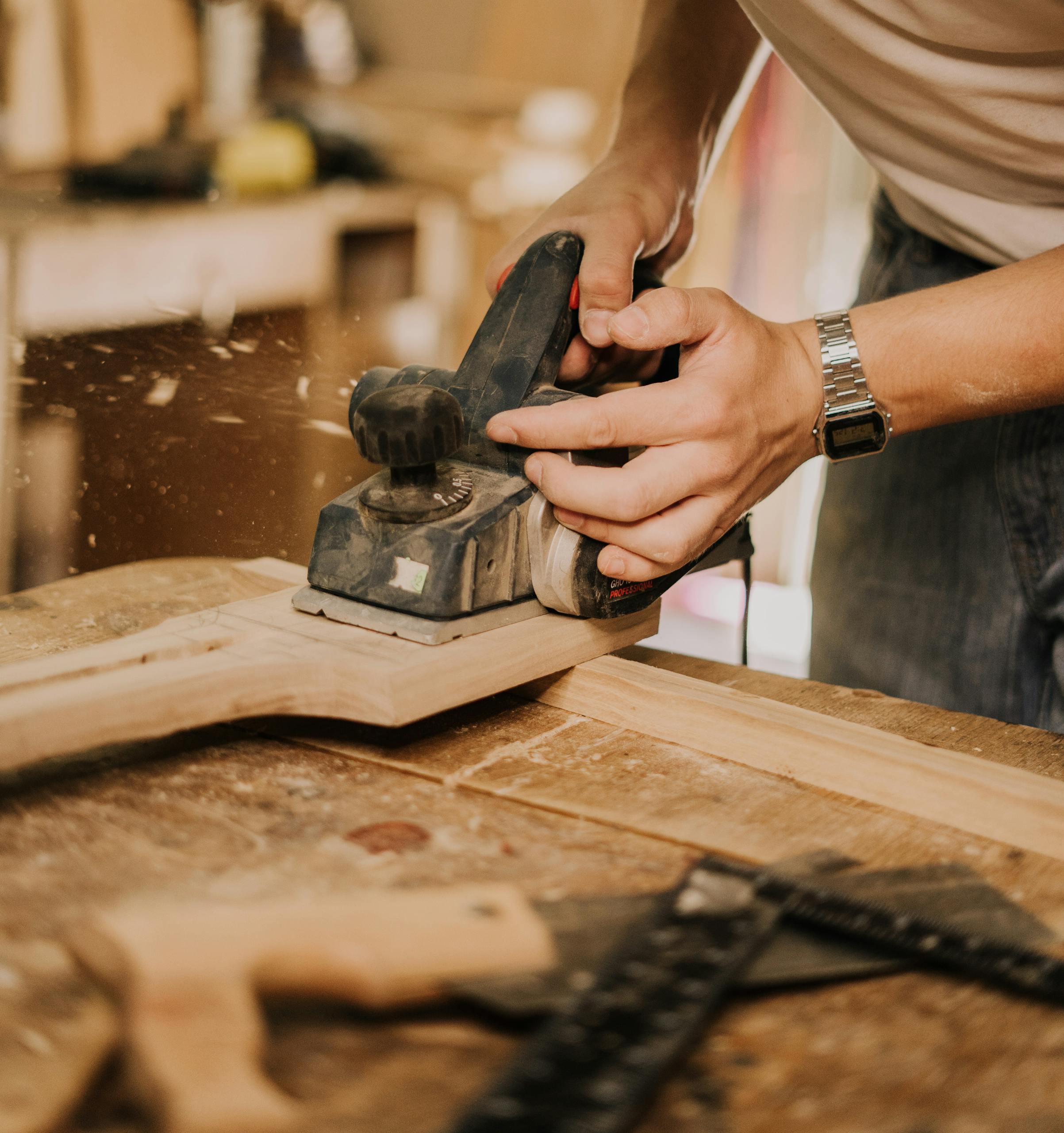 Close-up of a carpenter smoothing wood with an electric sander in a workshop.
