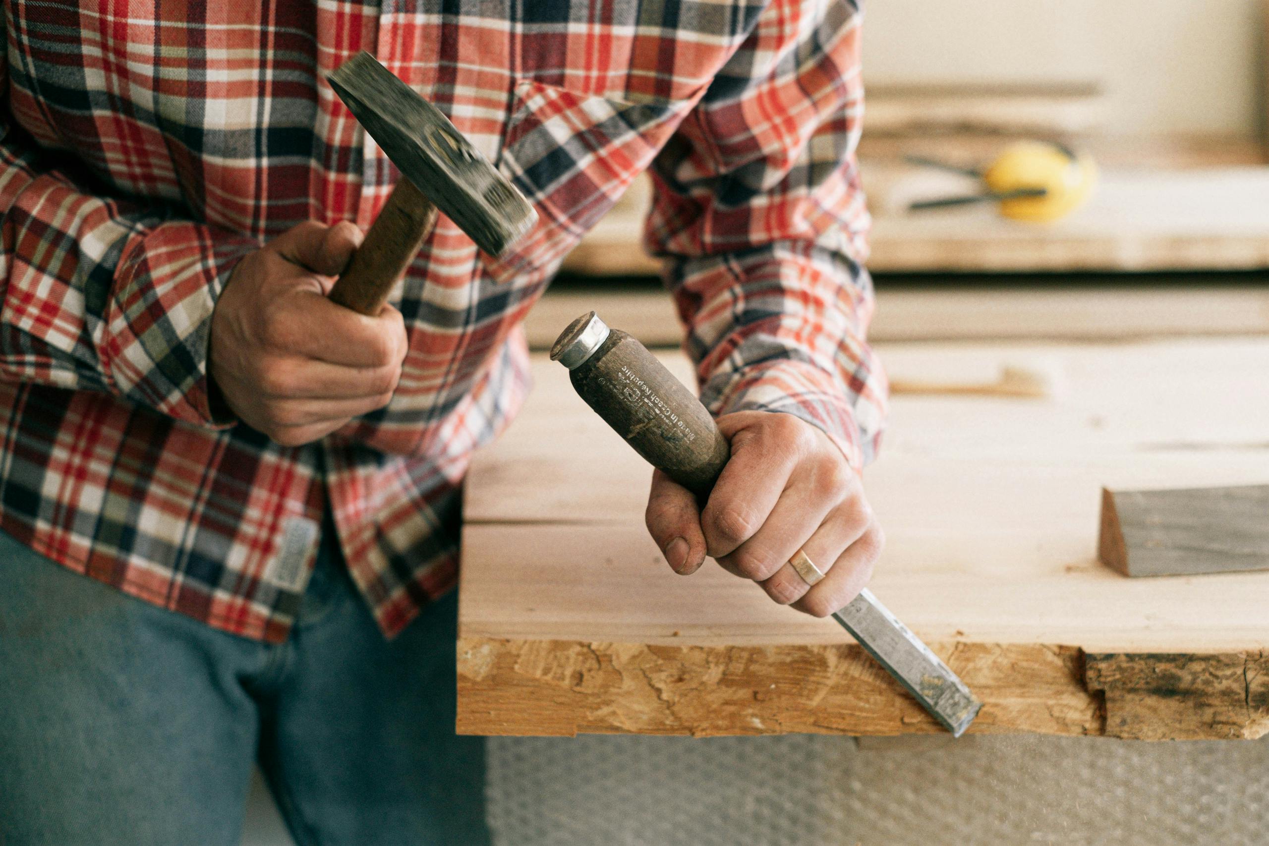 Detailed view of a carpenter using a hammer and chisel on a wooden plank, showcasing craftsmanship.